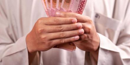 A man dressed in tradition white Muslim attire holds bank notes from South East Asia in his hands