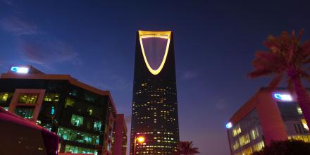 Illuminated Kingdom Centre Tower rises in Riyadh's urban landscape at twilight.
