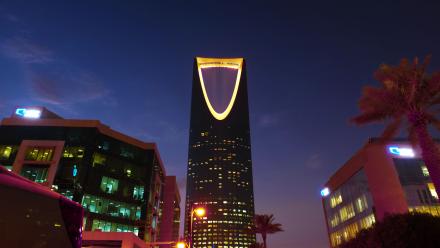 Illuminated Kingdom Centre Tower rises in Riyadh's urban landscape at twilight.