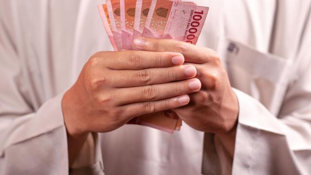 A man dressed in tradition white Muslim attire holds bank notes from South East Asia in his hands